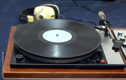 Vintage analogue classic style record player in wooden case with vinyl record with blue label and headphones. Horizontal photo front view closeup