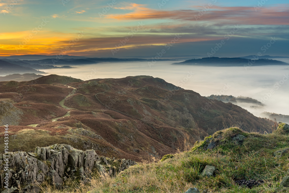 Beautiful Autumn sunrise from Loughrigg Fell in the Lake District with lovely lingering fog over the Cumbrian Valley.
