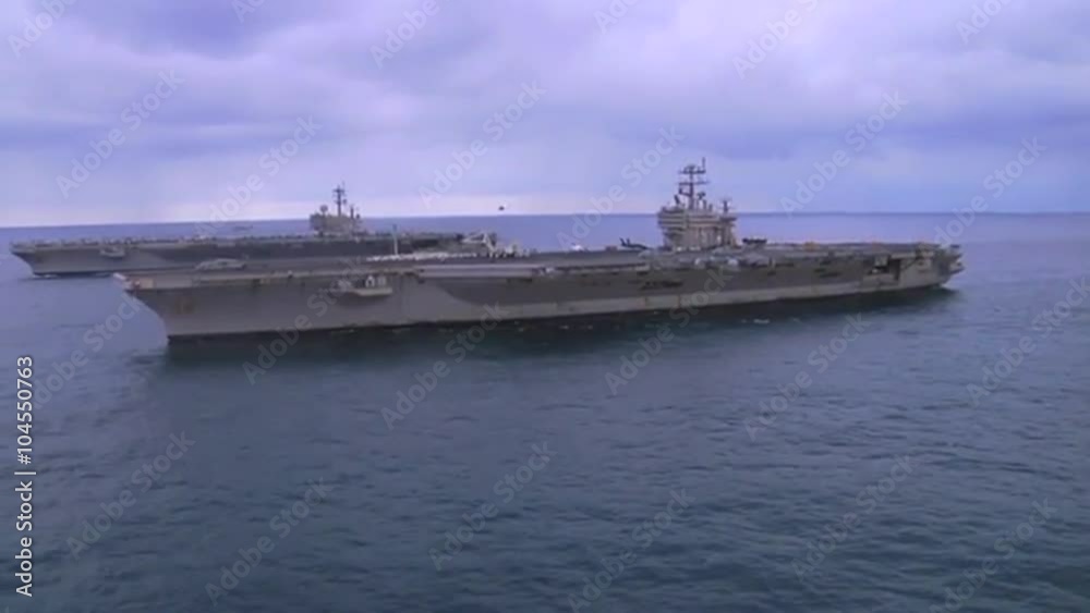 Aerial over two aircraft carriers on the high seas with helicopter moving between. Aerial over two aircraft carriers on the high seas with helicopter moving between.