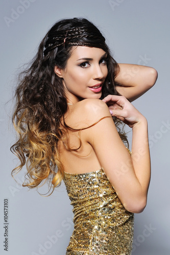 Portrait of a beautiful woman with trendy hairstyle wearing blue jeans and golden sparkling sequin top smiling happily