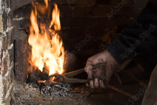 Fotografia, Obraz Close up of blacksmith heating metal piece in blacksmiths fire