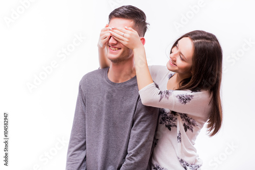 Attractive happy hipster woman with big toothy smile holding boyfriends eyes with surprise emotions. Smile girl look at happy man. Caucasian couple against white background.