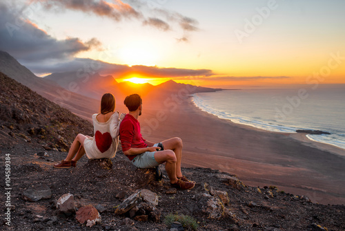 Young couple enjoying beautiful sunset sitting together on the mountain with great view on Cofete coastline on Fuerteventura island photo