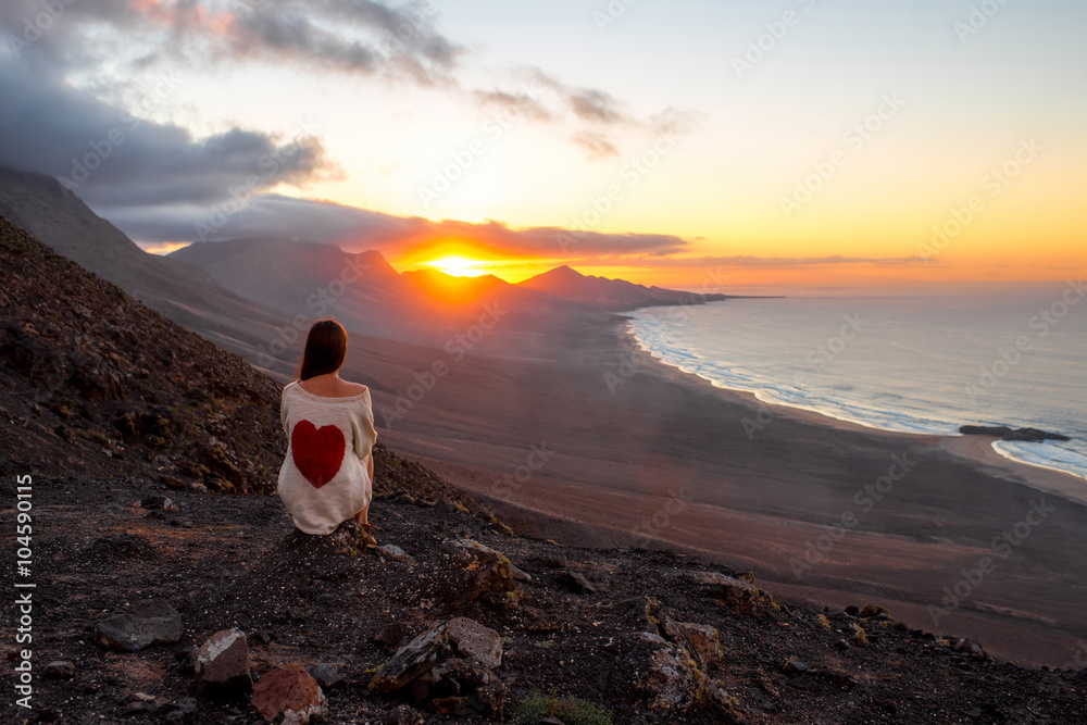 Fototapeta premium Young woman enjoying beautiful sunset sitting on the mountain with great view on Cofete coastline on Fuerteventura island