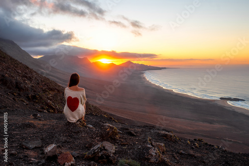 Young woman enjoying beautiful sunset sitting on the mountain with great view on Cofete coastline on Fuerteventura island photo