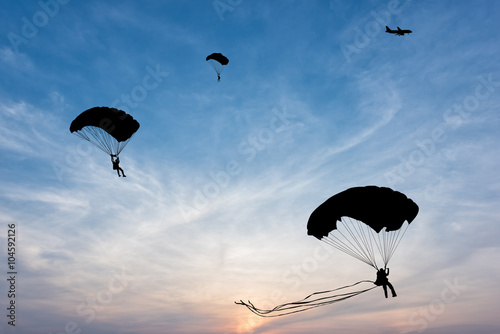 Silhouette of parachute and airplane on sunset background