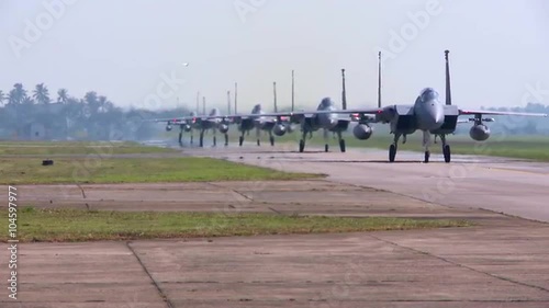 Numerous F-15 and F-16 fighter jets line up and taxi for takeoff in a military exercise.