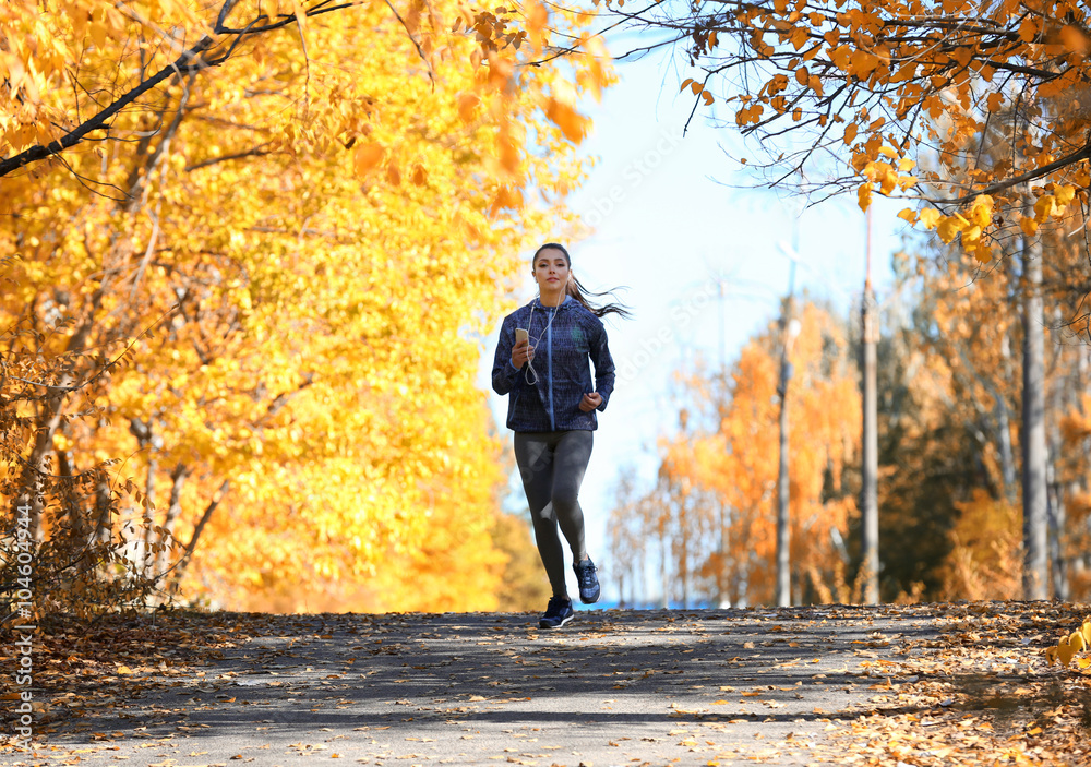 Young beautiful woman running in autumn park and listening to music with headphones.