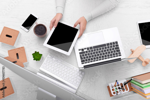 Concept of using electronics. Businesswoman works at office. Computer, laptop, tablet, cup of coffee and other things on the table. Top view