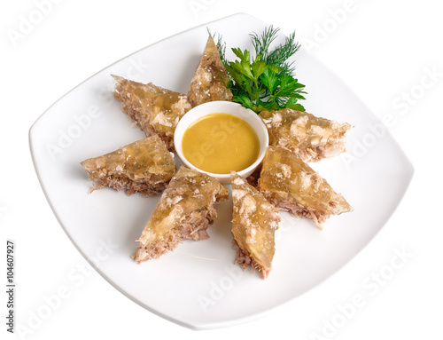 Sliced brawn with mustard in a gravy boat and greens on a square, isolated on white