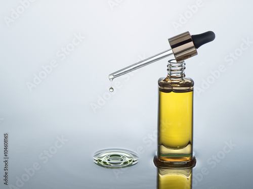 Moisturizing cosmetic oil stands on the dark water background with splash . The pipette with  oil drop lies on the bottle.