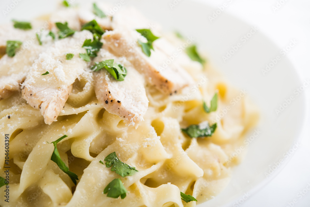 Pasta fettuccine alfredo with chicken, parmesan and parsley on white background close up. Italian cuisine.