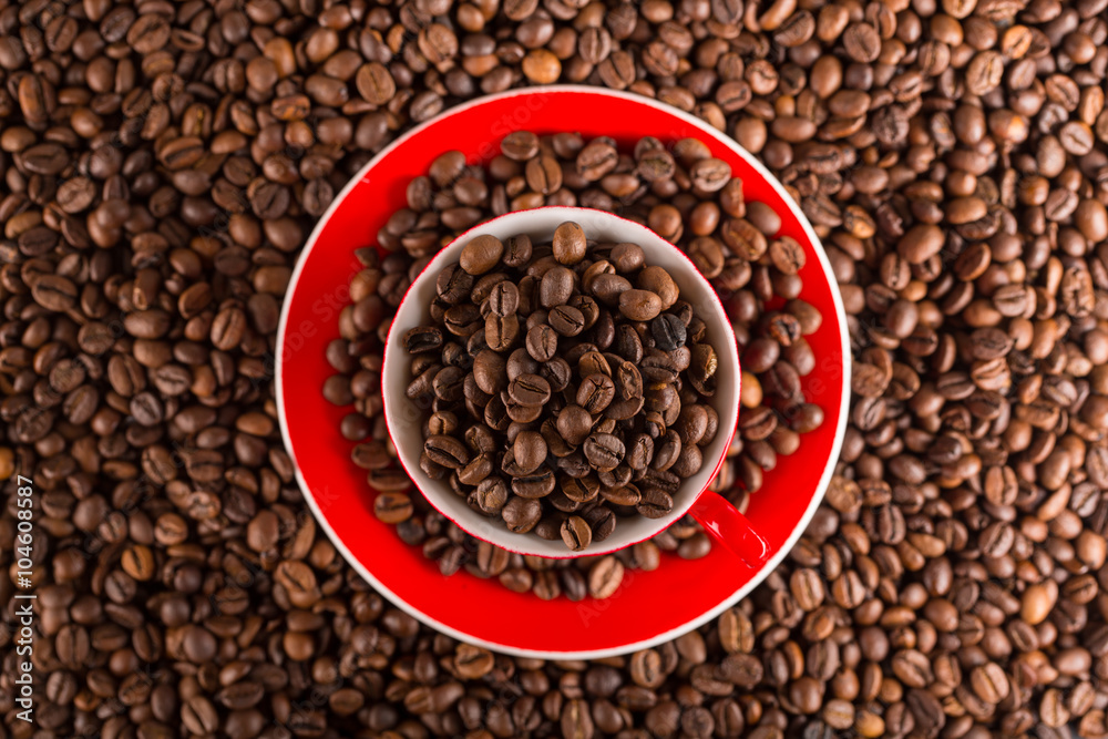 A red cup of coffee bean on the coffee beans background. Top view A red cup of coffee bean on the coffee beans background. Top view