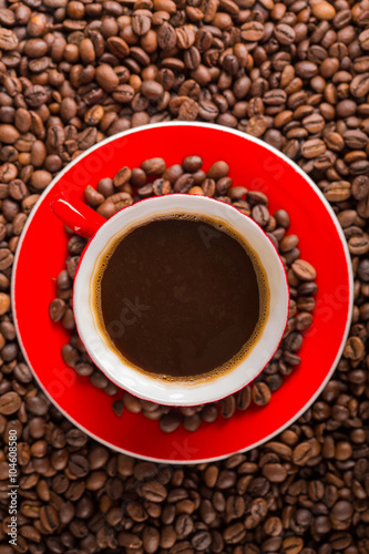 A red cup of coffee bean on the coffee beans background. Top view
