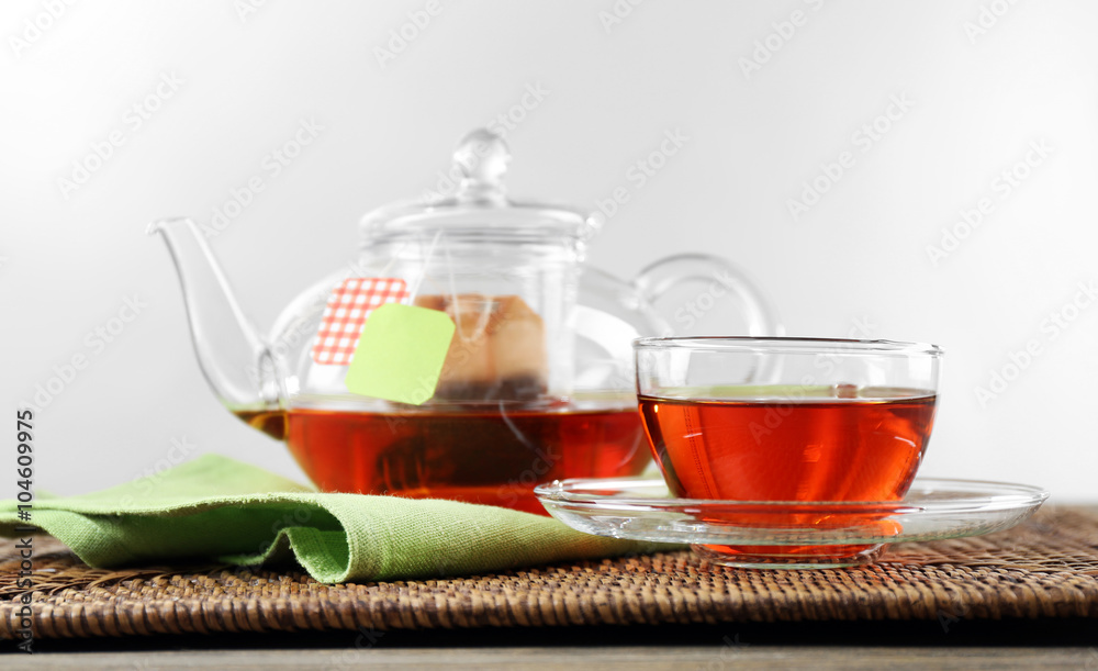 Fototapeta premium Cup of tea with tea bags and teapot on wooden background against grey background