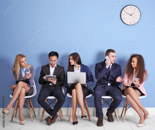 Young people sitting on a chairs and using devices in blue hall