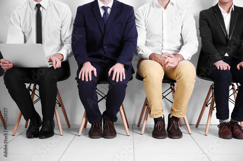 Young businessmen sitting on a chair in white hall, close up