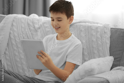 Boy using tablet on a sofa ...