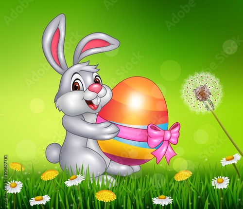 Cute little bunny holding easter egg on grass background 