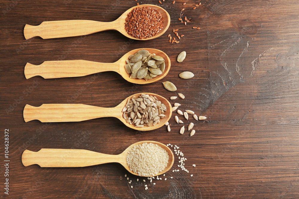 Sesame, flax, pumpkin and sunflower seeds in wooden spoons on table, closeup