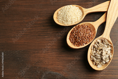 Sesame, flax and sunflower seeds in wooden spoons on table, closeup