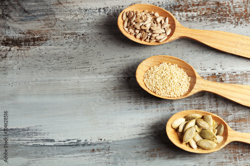 Sesame, pumpkin and sunflower seeds in wooden spoons on blue background, closeup