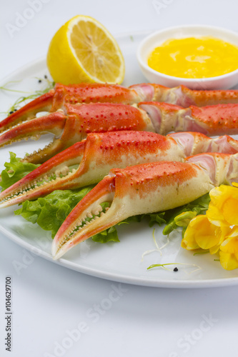 Boiled crab claws with sauce and lemon on a plate over white background