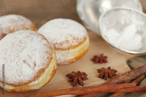 Delicious sugary donuts with spices on wooden cutting board closeup