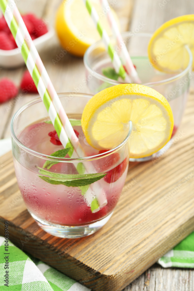 Raspberries and juice in glass on cutting board on grey wooden b Raspberries and juice in glass on cutting board on grey wooden b