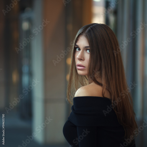 Beautiful brunette young woman in nice black dress. Posing on urban background. Fashion Photo