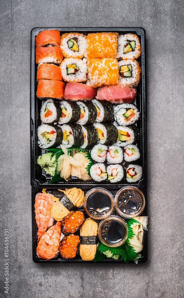 Various Sushi selection in black packaging tray on gray stone background, top view. Top view composing.  Japanese and Asian food.