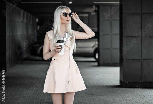 Blonde young woman posing with coffee outdoors