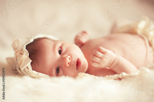 Cute infant girl lying in bed wake up close up. Looking at camera. Childhood. First days of new life. 