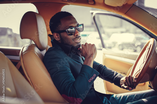 Blackman in sunglasses driving a car. © Fxquadro