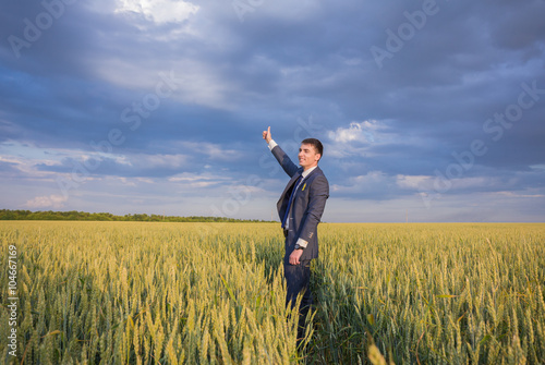 happy farmer, businessman, standing in wheat field over wind turbines background with his hands up and thumbs up © Ryzhkov Oleksandr