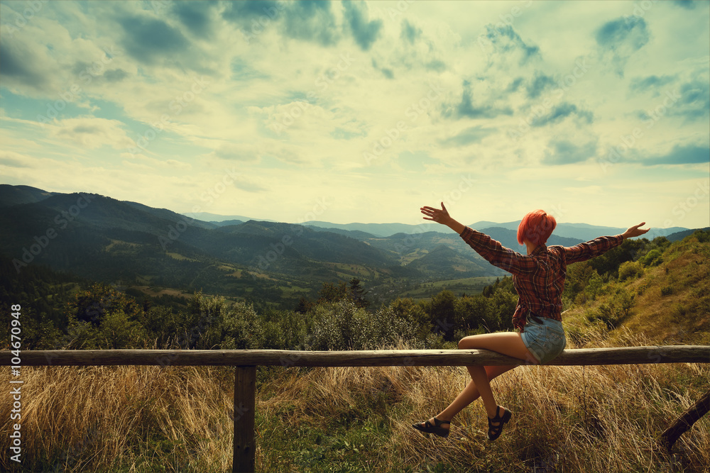 Fototapeta premium Young beautiful woman hiker enjoy the view at mountains. Model expressing joy and excitement with hands. Lady wearing stylish summer clothes.Toned