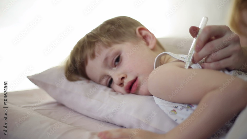 The boy is sick and he has fever and his mom measures his temperature using a thermometer
The boy is sick and he has fever and his mom measures his temperature using a thermometer