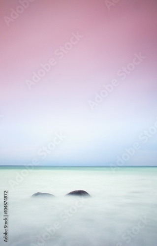 Romantic atmosphere in peaceful morning at sea. Big boulders sticking out from smooth wavy sea. Pink horizon photo