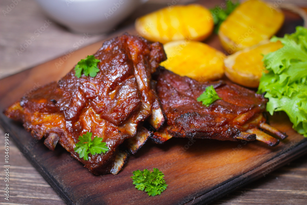Appetizing rosy and barbecued lamb ribs seasoned with a barbecue sauce and served with fresh herbs and potatoes on an old rustic wooden chopping board