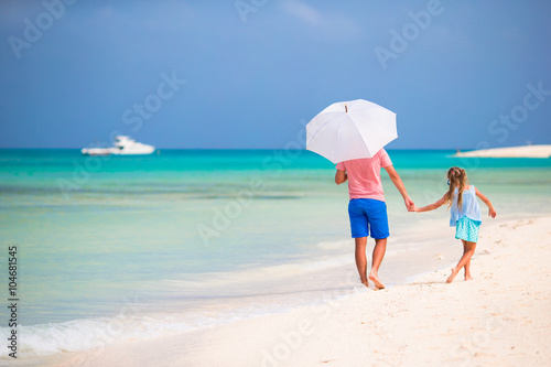 Father and daughter at beach with umbrella to hide from sun