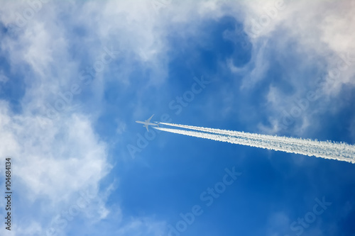 Silhouette of aircraft flying in the clouds and leaving contrail