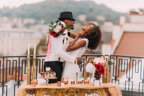 Stylish african wedding couple having fun on the balcony with luxury golden table in oriental style on foreground