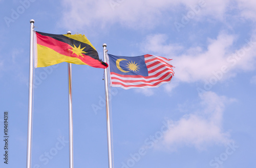 Malaysian flag, the Jalur Gemilang or Stripes of Glory next to a Sarawakian flag on tall flag poles on a windy day photo