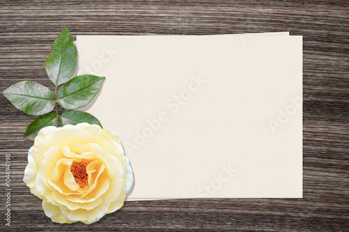 Yellow rose and and paper on wood background