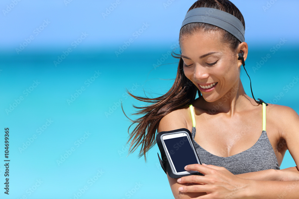Fit woman using smartphone app on armband. Young Asian female runner touching the display on sports arm strap with mobile phone for listening to music or as activity tracker. Stock