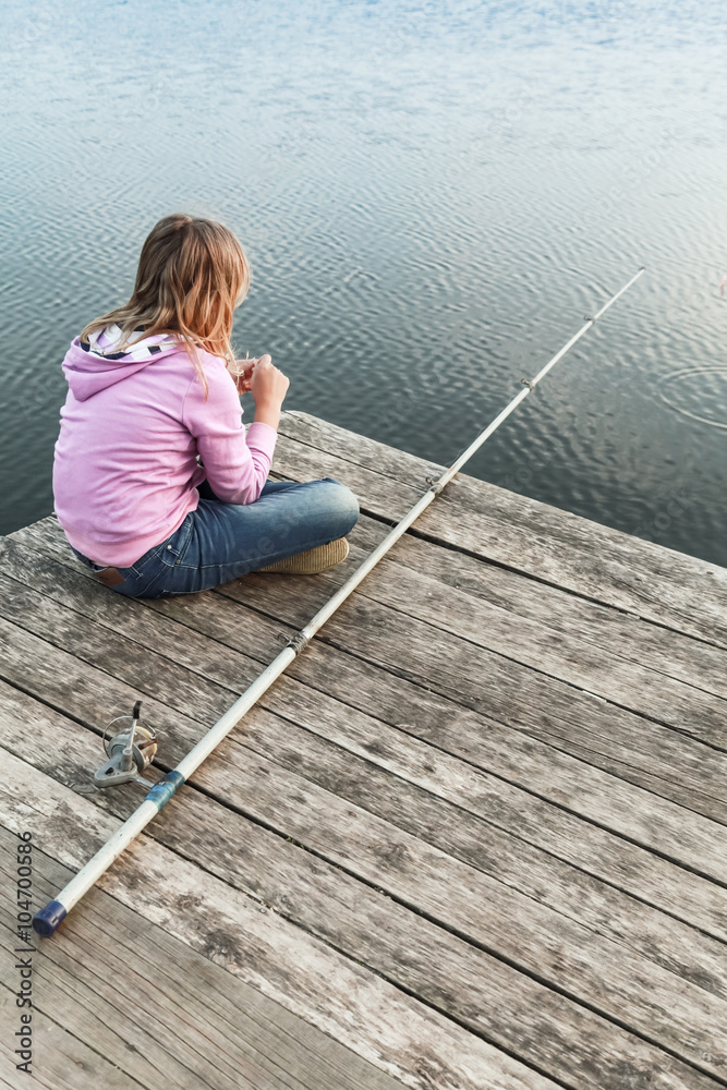 Little blond girl sitting on a pier with fishing rod