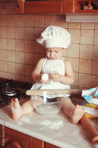 Little scullion is kneading dough in an apron and chef's hat sitting in the flour.