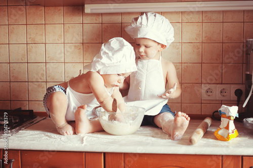 Two little boys cook play dough on the table in an apron and chef's hat