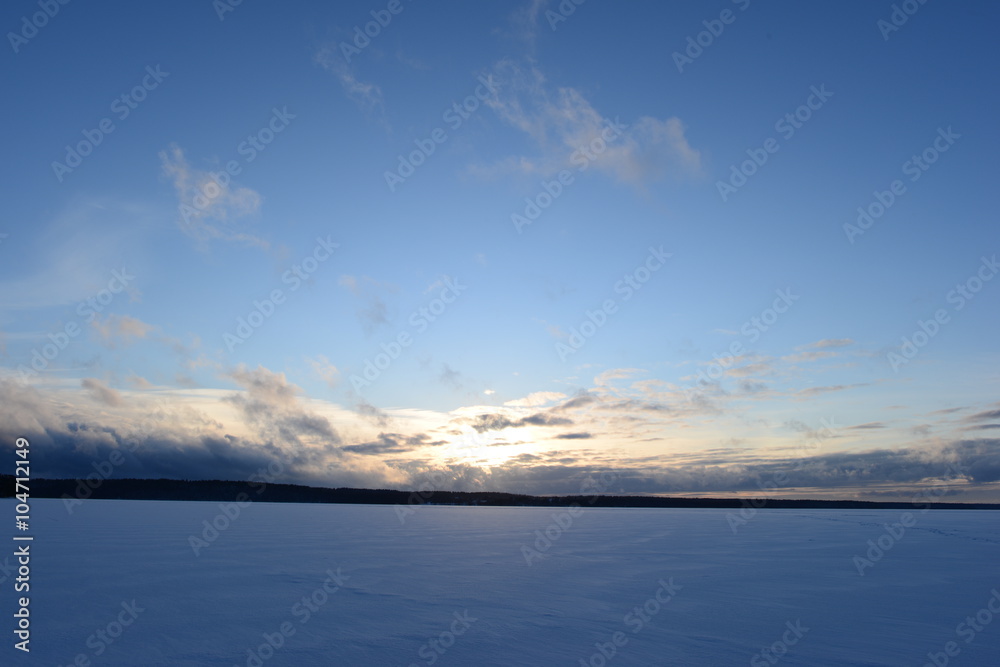 Sunset on a snowy winter lake in a cloudless blue sky