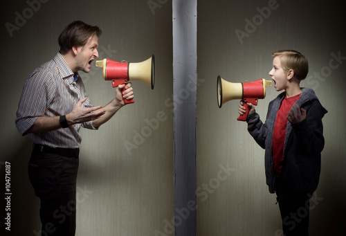 Tween son and his father yelling through the megaphones standing on either side of a wall photo